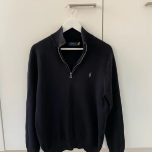 Svart tröja från Ralph Lauren - Snygg svart tröja från Ralph Lauren med dragkedja vid halsen. Tröjan har långa ärmar och en diskret logga på bröstet. Perfekt för en stilren look. Kan tänka mig byta mot full zip