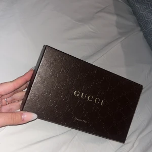 Svart plånbok från Gucci - Elegant svart plånbok från Gucci med präglat mönster och guldfärgad detalj. Plånboken har flera fack för kort och en dragkedja för mynt. Perfekt för att hålla ordning på dina värdesaker med stil.
