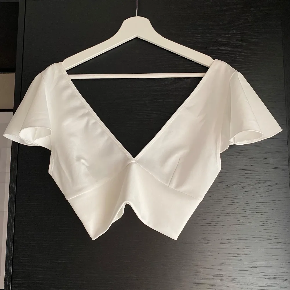Säljer en superfin vit croppad topp med djup v-ringning och korta ärmar. Perfekt för sommardagar eller en utekväll. Toppen har en elegant och stilren design som passar till både jeans och kjol.. Yläosat.