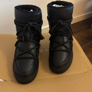 Svarta vinterboots med snörning - Säljer ett par svarta vinterboots från Inuikii i full läder. De har en hög design med snörning framtill och en mysig insida som håller fötterna varma. Perfekta för kalla vinterdagar och ger en stilren look. Använda ute endast en gång och är som nya.