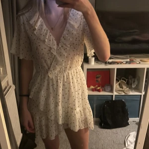 Vit prickig klänning från Zara - Charmig vit klänning från Zara med svarta prickar och volangdetaljer. Klänningen har en omlott-design och korta ärmar, perfekt för en somrig look. Tillverkad i ett lätt och luftigt material. Skriv för mer information💕
