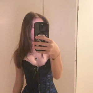 Blå korsett med svarta detaljer - Snygg blå korsett med svarta spetsdetaljer och snörning framtill. Perfekt för en kväll ute eller en speciell tillställning. Korsetten har en elegant och figurnära passform.