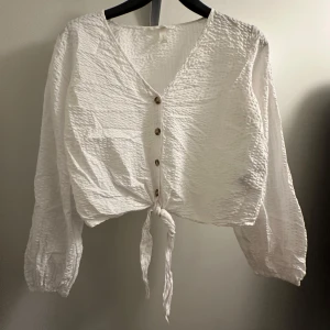 Vit topp - En vit långärmad topp från hm i storlek 40. Har fina knappar framtill och snören att knyta hur man vill! Helt oanvänd. 
