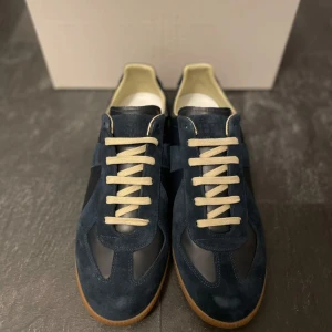 Maison Margiela Skor - Säljer ett par snygga mörblåa Maison Margiela i mocka med vita snören. De har en stilren design och en bekväm gummisula. Skorna är i mycket skick, box och dust bag ingår. Finns även kvitto!