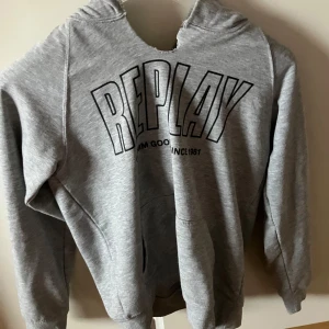 Grå hoodie från Replay - Säljer en snygg grå hoodie från Replay i bra skick. Den har en stor logga på framsidan och en praktisk magficka. Perfekt för höst och vinter, och den är superbekväm att ha på sig. Passar både till vardags och chillkvällar. Hör av dig om du är intresserad!