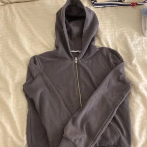 Grå hoodie med dragkedja - Säljer en grå hoodie i bra skick. Den har en dragkedja framtill och en mysig huva. Perfekt för höst och vår när det är lite kyligt ute. Passar både till vardags och chillkvällar. Storleken är inte angiven, men den ser ut att ha en normal passform.