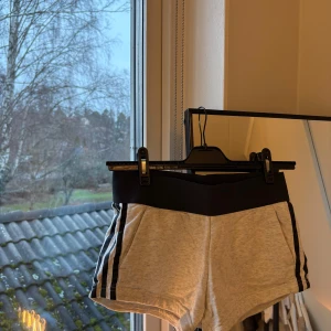 Grå shorts från Adidas - Säljer ett par grå shorts från Adidas i storlek XS. De har en bekväm svart resårmidja och klassiska svarta ränder längs sidorna. Perfekta för träning eller en avslappnad dag. Materialet känns mjukt och skönt