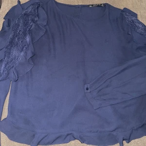 mörkblå blus med spetsdetaljer (liten i storlek) - en elegant mörkblå blus med långa ärmar och vackra spetsdetaljer längs axlarna. blusen har volanger och knappar på baksidan. perfekt för både vardag och fest! (OBS!! väldigt liten i storleken, passar mig som har S)