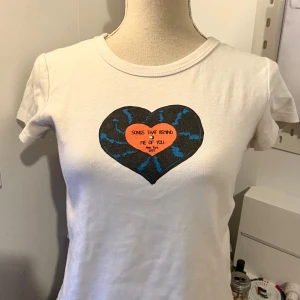 Vit t-shirt  - Säljer en vit t-shirt från Cider i storlek S. Den har ett coolt hjärtmotiv med texten 'Songs that remind me of you, New York 1997' i mitten. Perfekt för en casual look eller en avslappnad dag ute. T-shirten är i bomull och har en normal passform.