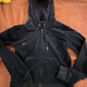 Mörkblå hoodie från Juicy Couture - Säljer en snygg mörkblå hoodie från Juicy Couture. Den har en dragkedja framtill och en justerbar huva med snörning. Perfekt för en avslappnad stil.