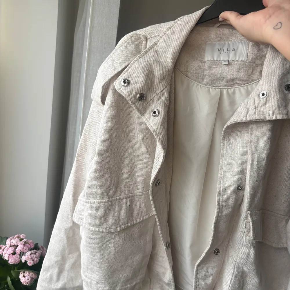Snygg beige jacka från Vila med dragkedja och knappar. Perfekt för vår och höst med sin stilrena design och långa ärmar. Jackan har en normal passform och är tillverkad i ett bekvämt material.. Takit.