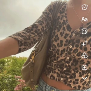 Leopardmönstrad blus med knappar - Trendig leopardmönstrad blus med v-ringning och knappar framtill. Blusen har trekvartsärmar och en figurnära passform, perfekt för en stilfull look.