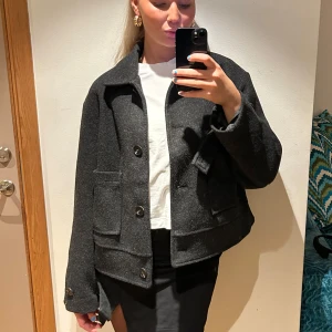 Mörkgrå kavajjacka - Snygg mörkgrå kavajjacka med knappar framtill och klassisk krage. Jackan har en normal passform och är perfekt för höst och vår. Den har långa ärmar och praktiska fickor.