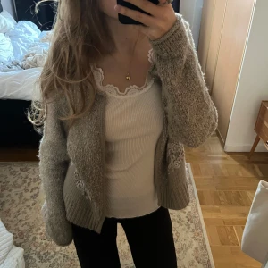 Stickad kofta med broderade detaljer - Mysig beige/grå stickad kofta med fina broderade detaljer på framsidan. Den har ribbstickade muddar vid ärmslut och nederkant. Perfekt till vinter.🤍Kontakta vid frågor 🌸