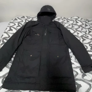 Svart Sail racing/gortex jacka - Snygg svart parkajacka med huva och dragkedja. Jackan har praktiska fickor med knappar och en stilren design. Perfekt för kyligare dagar. Storlek L