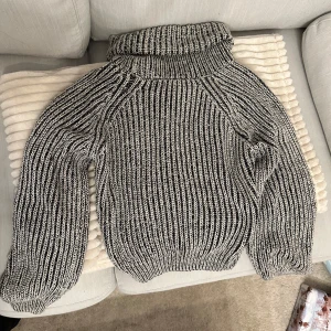 Grå och vit stickad polotröja  - Mysig grå och vit stickad polotröja med ribbat mönster från bikbok. Perfekt för kyliga dagar med sin höga krage och långa ärmar. Tröjan har en avslappnad passform och är idealisk för både höst och vinter.