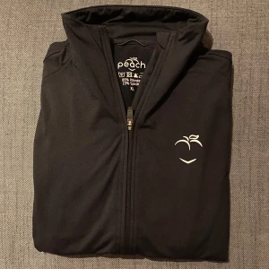 Svart träningsjacka från Peach  - Säljer en svart jacka från Peach Athletics i storlek XL, passar M-XL. Jackan har en dragkedja framtill och en stilren design med en liten logotyp på bröstet samt bak. Perfekt för träning eller till vardags också. Använd men i mycket bra skick. 