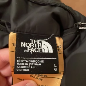 Svart pufferjacka från The North Face - Säljer en svart pufferjacka från The North Face i storlek L. Jackan är perfekt för kalla dagar med sitt quiltade mönster och långa ärmar. Den har en dragkedja och en huva för extra värme. Passar både för vardag och utomhusaktiviteter. 🖤Du kan även vända ut och in på den så blir det en reflex jacka men du kan också ha vanligt du ser hur båda ser ut på bild