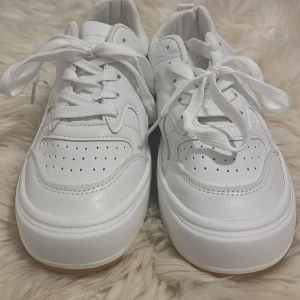 Vita sneakers med snörning - Snygga vita sneakers med klassisk snörning och perforerade detaljer på ovansidan. Skorna har en stilren design med en tjock sula som ger extra komfort. Perfekta för en avslappnad stil. Kommer med tillhörande kartong! 