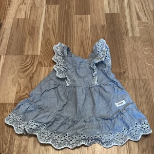 Blå klänning från Newbie - Söt blå klänning från Newbie med broderade detaljer och volanger. Klänningen har knappar bak och är ärmlös, perfekt för små äventyrare. Passar barn i åldern 6-9 månader.