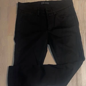 Svarta jeansbyxor - Snygga svarta jeansbyxor med en klassisk design. De har en tight passform och är perfekta för en stilren look. Byxorna har fickor både fram och bak samt en knapp och dragkedja i midjan.