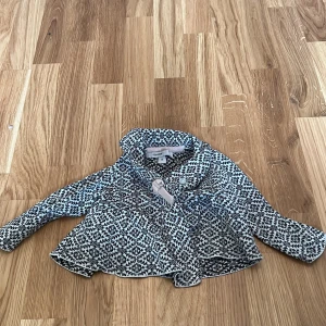 Mönstrad kofta från Mywear Baby - Söt och mysig kofta från Mywear Baby i storlek 74. Den har ett fint svartvitt mönster och långa ärmar. Perfekt för att hålla de små varma under kyligare dagar.