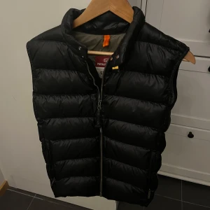 Svart dunväst från Parajumpers - Säljer en snygg svart dunväst från Parajumpers i mycket bra skick. Västen är perfekt för vår och höst och har en stilren look. Storlek Y-M(160-170). Nypris 3700kr mitt pris 1150kr. Kan kanske gå ner lite i priset vid snabbaffär.