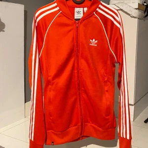 Röd träningskofta från Adidas - Snygg röd träningskofta från Adidas. Använd ett par gånger men bra skick! Skriv! 