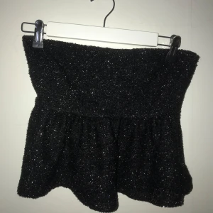 glittrig topp - Snygg svart glittrig topp. Toppen är axelbandslös och har en volangdetalj nedtill. Perfekt festtopp eller inför nyår
