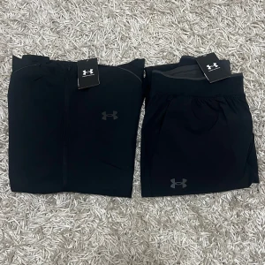 Under Armour tracksuit  - Säljer en svart träningsjacka från Under Armour i nytt skick. Jackan har en dragkedja framtill och en praktisk huva. Perfekt för träning eller som en lätt jacka under höst och vår. Den är långärmad och har en stilren design med Under Armour-loggan på bröstet och ryggen. (KVITTO FINNS)