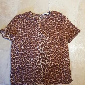 Leopardmönstrad topp från Samsøe Samsøe - Snygg leopardmönstrad topp från Samsøe Samsøe i ett mjukt material. Toppen har korta ärmar och en rund halsringning. Perfekt för en trendig vardagslook eller en utekväll. Den har en liten knappdetalj i nacken för enkel på- och avtagning.