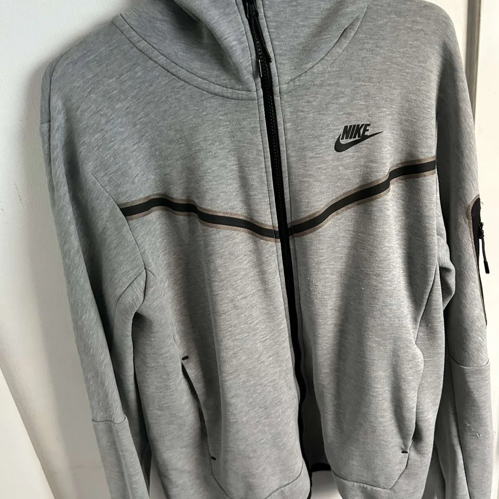 Säljer en grå hoodie från Nike i bra skick. Den har en dragkedja framtill och en svart randdetalj över bröstet. Perfekt för höst och vår, med långa ärmar och en bekväm passform. Huvan ger extra mysfaktor. Passar både till träning och vardag.. Jackor.