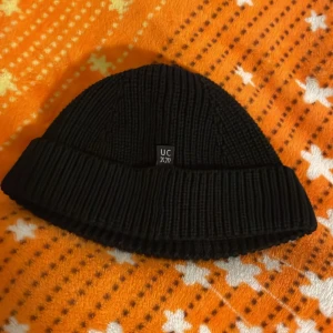 Svart ribbad mössa från Urban Collective - Säljer en snygg svart ribbad mössa från Urban Collective. Perfekt för kalla dagar med sin stilrena design och varma material. Mössan har en liten etikett framtill och är i mycket bra skick. Passar perfekt till både vardag och fest!