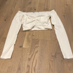 Vit offshoulder topp - Snygg vit offshoulder topp i ribbat material. Den är croppad och har långa ärmar, perfekt för en stilren look. Passar både till vardags och fest!