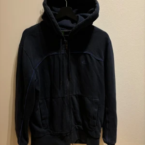 Mörkblå huvtröja från Hugo Boss - Säljer en snygg mörkblå huvtröja från Hugo Boss i mycket bra skick. Tröjan har en dragkedja framtill och är långärmad med en bekväm passform. Perfekt för höst och vår, och den är gjord av bomull vilket gör den supermjuk och skön att ha på sig. Passar både till vardags och lite mer avslappnade tillfällen. 