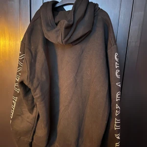 Svart hoodie med tryck från hm, märke Daily Basis - Säljer en svart hoodie med coolt tryck på framsidan och texten 'DAILY BASIS' längs ärmarna. Perfekt för en avslappnad stil och passar till alla tillfällen. Den har en stor ficka fram och en bekväm huva. Perfekt för höst och vinter!