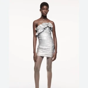 Silver axelbandslös klänning från Zara - Snygg silverfärgad klänning från Zara i axelbandslös design med volangdetaljer upptill. Perfekt för nyår!! Aldrig använt, därför säljer jag för original pris, men kan diskutera priset!! Om man vill se klänning på är det bara och fråga om bild🫶🏽