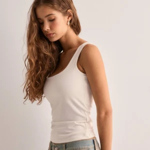 Vit ärmlös linnetopp - Snygg och enkel vit linnetopp i bomull från Nelly. Aldrig använt, bara testat. Perfekt för sommardagar eller som ett basplagg i garderoben. Toppen har en tight passform och är ärmlös, vilket gör den både bekväm och stilren. Original pris: 180 kr