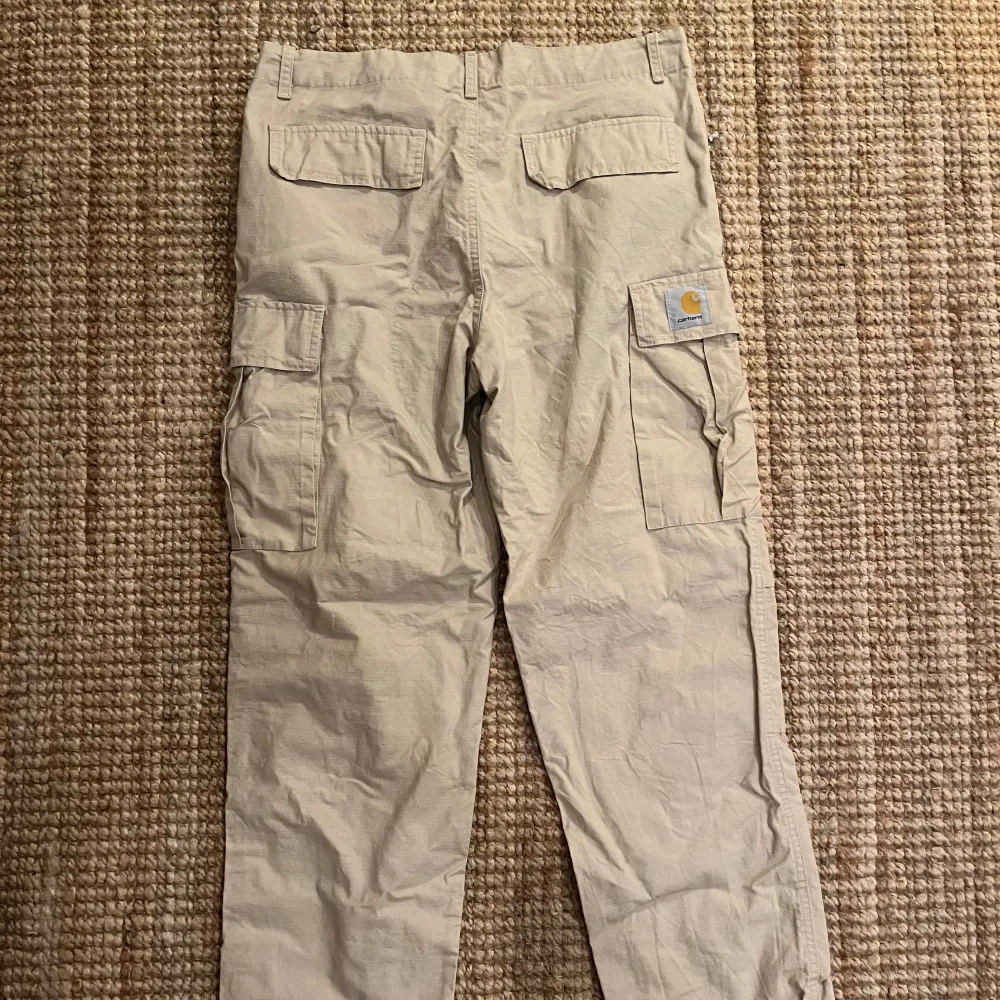 Säljer ett par beige cargobyxor från Carhartt i storlek M, men passar som S. Byxorna har flera praktiska fickor och är perfekta för en avslappnad stil. Tillverkade i slitstarkt material, idealiska för både vardag och utomhusaktiviteter.. Jeans & Byxor.