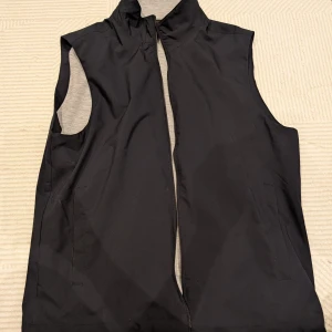 Marinblå väst/gilet från Mango i M - Säljer en stilren marinblå väst med dragkedja från Mango i stl M. Perfekt för lager-på-lager under höst och vår. Västen har en hög krage och är fodrad med grått tyg på insidan. Den är i mycket bra skick och passar både till vardags och träning. 