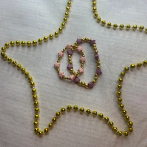 Färgglada armband med stjärnor - Säljer två supergulliga armband med stjärnor! Ett armband har lila stjärnor och det andra har rosa stjärnor, båda med gyllene pärlor emellan. Perfekta för att liva upp vilken outfit som helst. Passar både till vardag och fest! 🌟