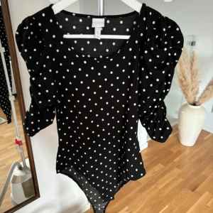 Svart prickig body - Säljer en superfin svart body med vita prickar. Den har puffiga långärmar och en bekväm passform. Perfekt för både vardag och fest! 🖤
