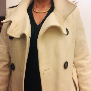 Beige ullkappa med bälte - Säljer en elegant beige kappa i mycket bra skick. Den har en klassisk design med knappar och ett bälte i midjan för en snygg passform. Perfekt för höst och vår! 🧥