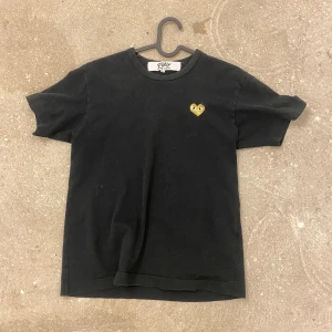 Svart t-shirt från Comme des Garçons - Säljer en svart t-shirt från Comme des Garçons med ett guldhjärtat T-shirten är i bomull och har en normal passform.