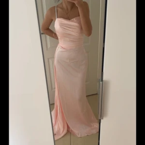 Ljusrosa långklänning som är satin  - Elegant ljusrosa långklänning i satin  och draperad överdel. Klänningen har en vacker slits  framtill som ger en extra touch av glamour. Perfekt för bal eller fest!