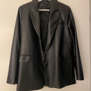 Svart skinnkavaj - Snygg svart skinnkavaj från Chiquelle i mycket bra skick. Den har en klassisk design med långa ärmar och knappar på ärmsluten. Perfekt för både fest och vardag. Passar till det mesta och ger en cool touch till din outfit. (Kavajen har ett hål i innertyget, det är inget som syns när man har den på sig och går säkert att sy ihop om man skulle vilja)