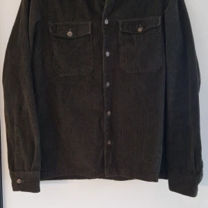 Mörkgrön manchesterskjorta från Jack & Jones - Säljer en snygg mörkgrön manchester skjorta från Jack & Jones i storlek XS. Knappar framtill samt två bröstfickor med knappar. Perfekt för höst och vår! 🧥
