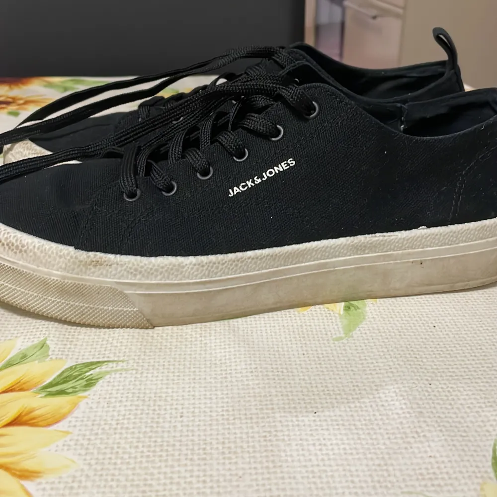 Säljer ett par svarta sneakers från Jack & Jones i bra skick. De har en klassisk design med snörning och en vit sula som ger en snygg kontrast. Perfekta för vardagsbruk och passar till det mesta i garderoben.. Skor.