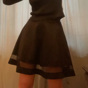 Svart kjol med genomskinlig rand - Svart stretchig kjol med en rand i mesh. Har några noppor på baksidan, men de syns bara på nära håll (se bild 5). Midja 33 cm outtöjd. Längd 48 cm.