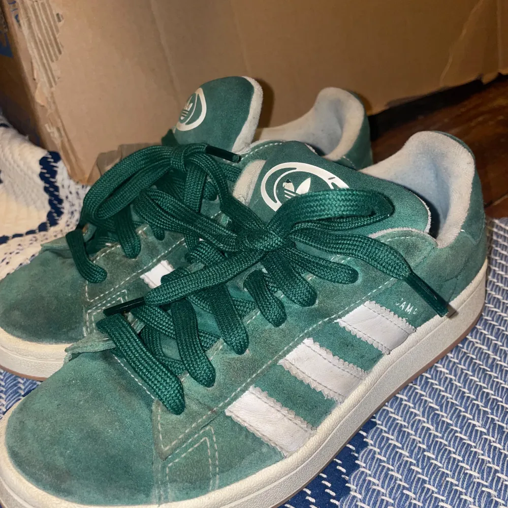 Säljer ett par gröna Adidas sneakers i mocka med vita detaljer. De har klassiska tre ränder på sidan och snörning framtill. Skorna är i bra men använt skick , bilderna visar defekt. Går säkert att fina till efter lite tvätt m.m för den som vill/orkar. Storlek 38. Skor.